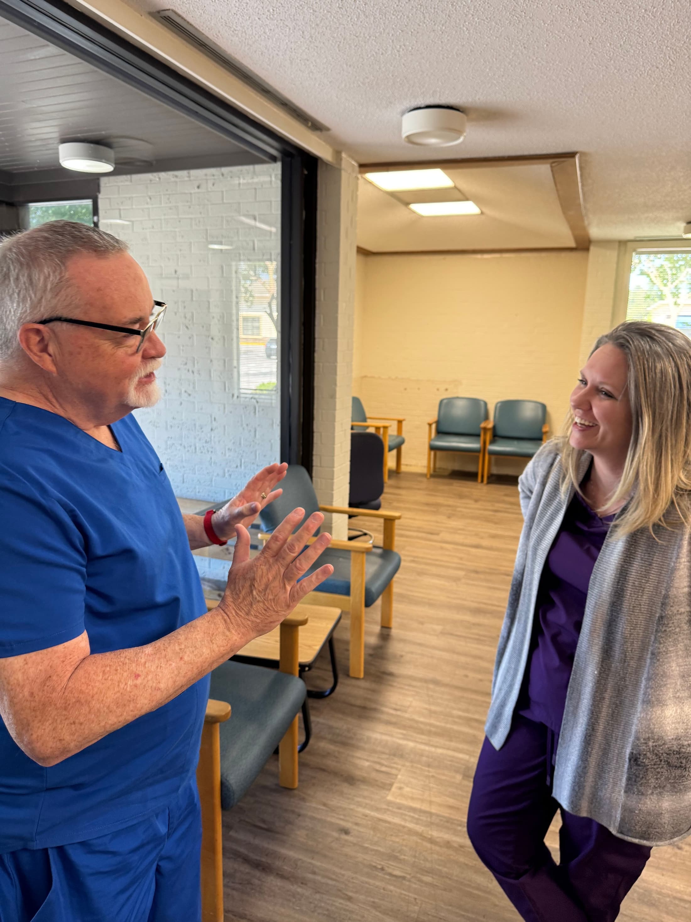 Two members of the MERCI Clinic team in scrubs share a laugh in the waiting room.